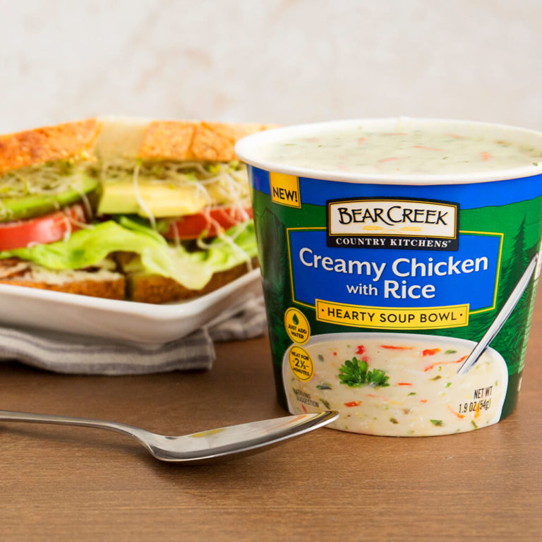Bear Creek Creamy Chicken with Rice soup bowl next to a fresh sandwich on a wooden table.