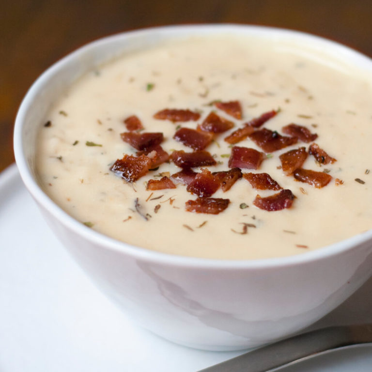 Creamy potato soup topped with bacon bits and herbs in a white bowl.