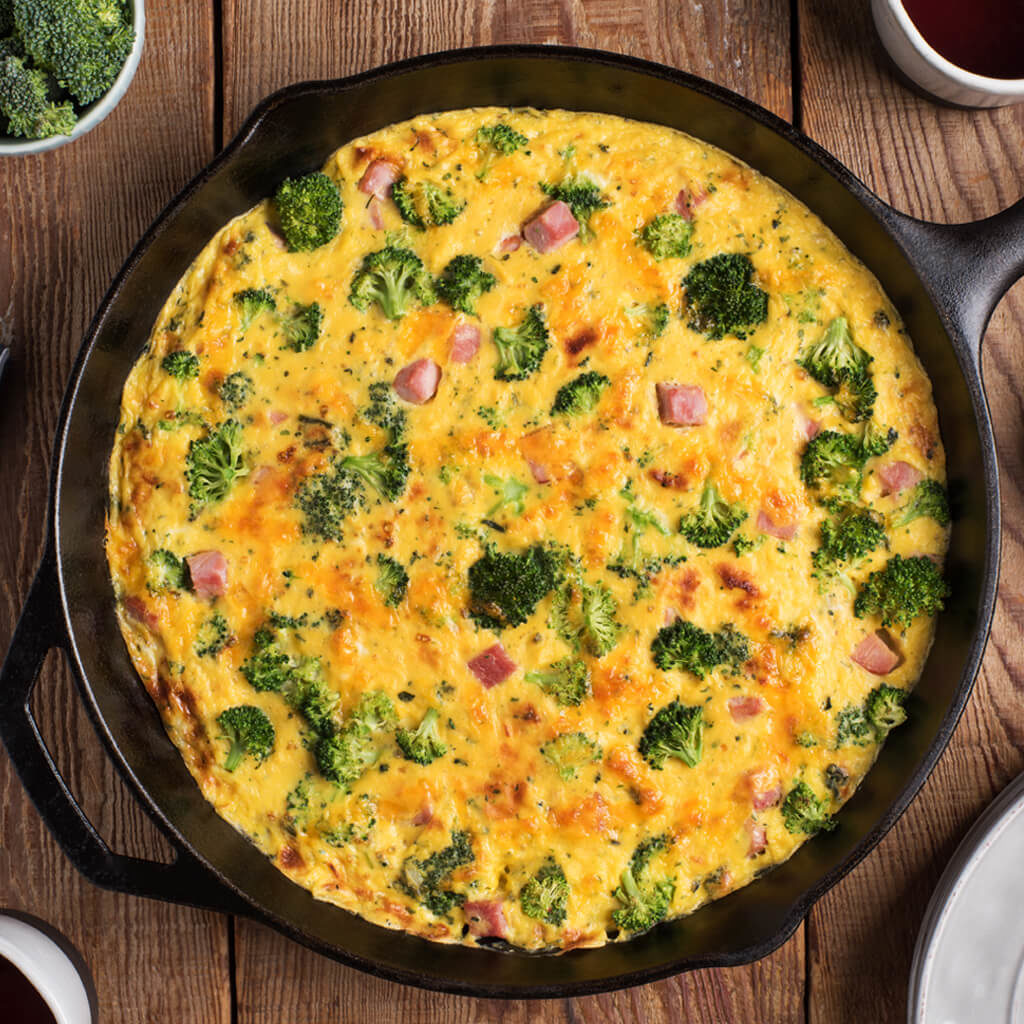 Broccoli and ham frittata in a cast iron skillet on a wooden table.