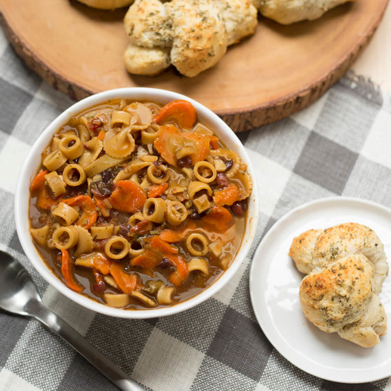 Homemade minestrone soup with carrots and pasta served with garlic bread on a wooden table.