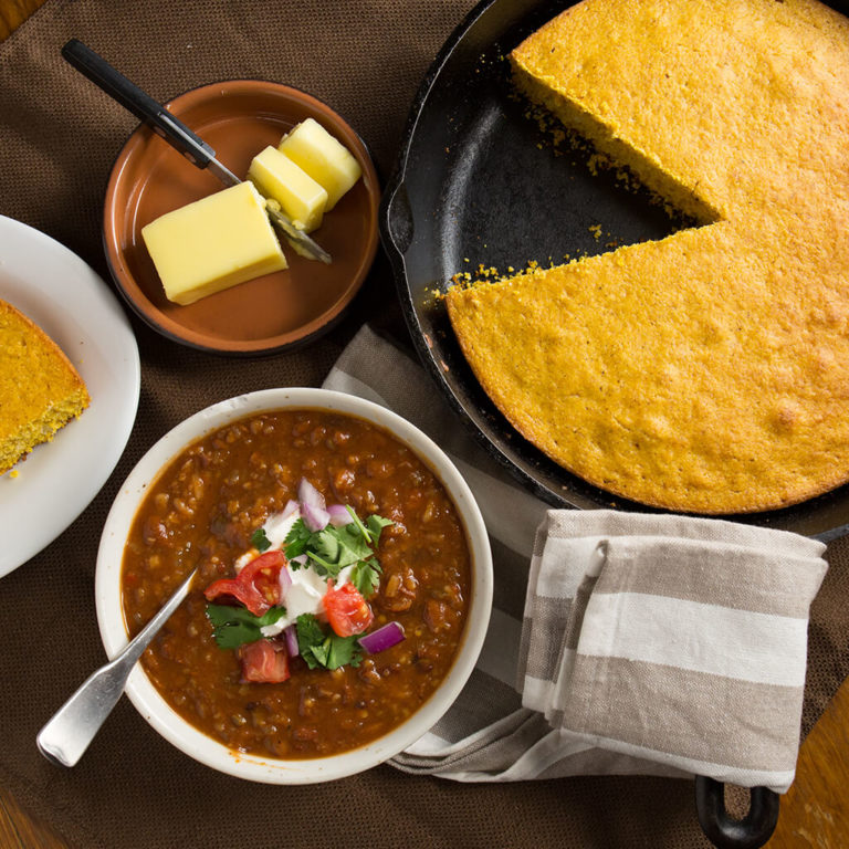 Delicious homemade chili with fresh toppings and golden cornbread in a cast iron skillet on a rustic table.
