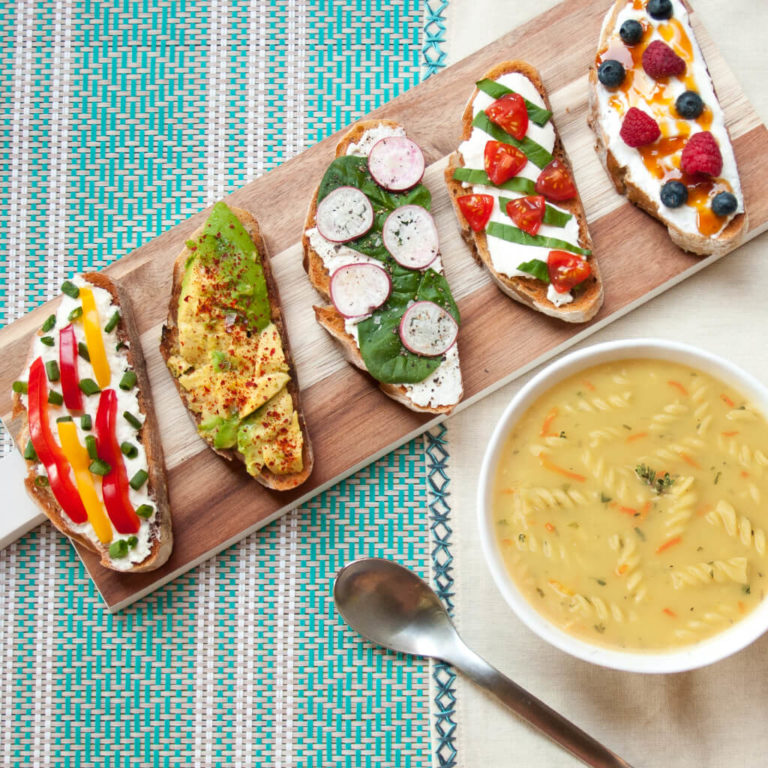 Assorted gourmet toasts and bowl of soup on a patterned tablecloth.