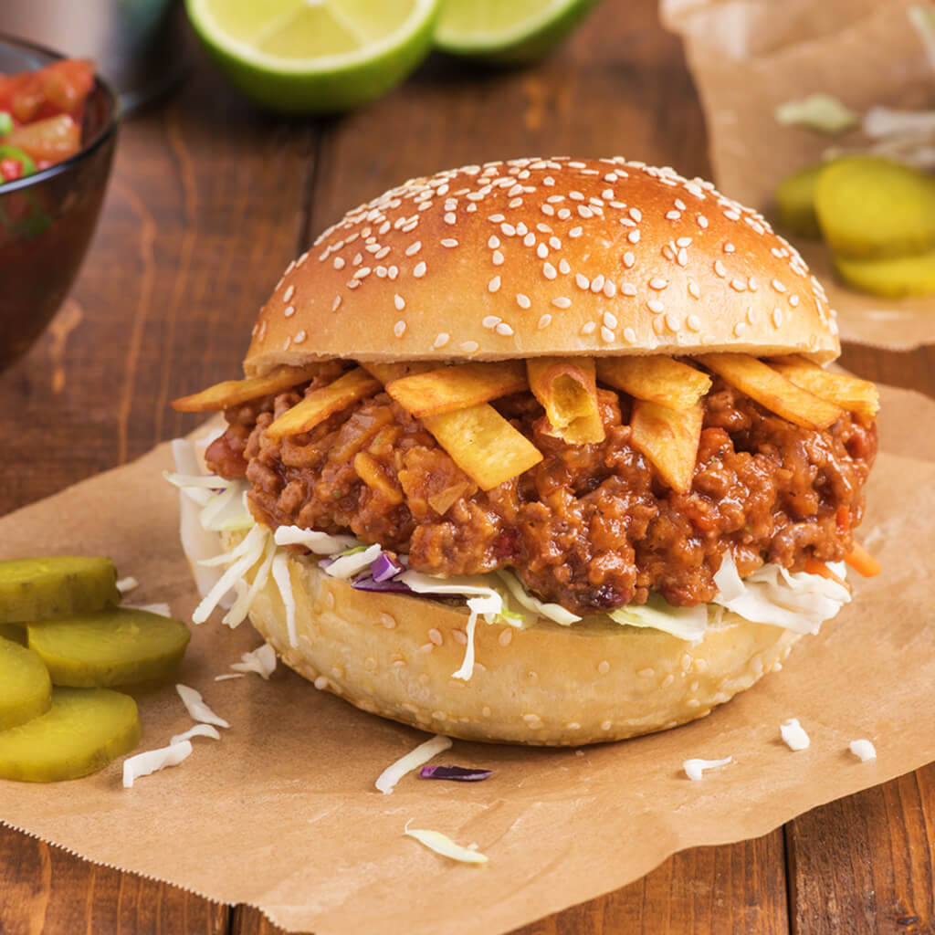 Juicy sloppy joe with crispy fries on a sesame bun, served with pickles on a wooden surface.