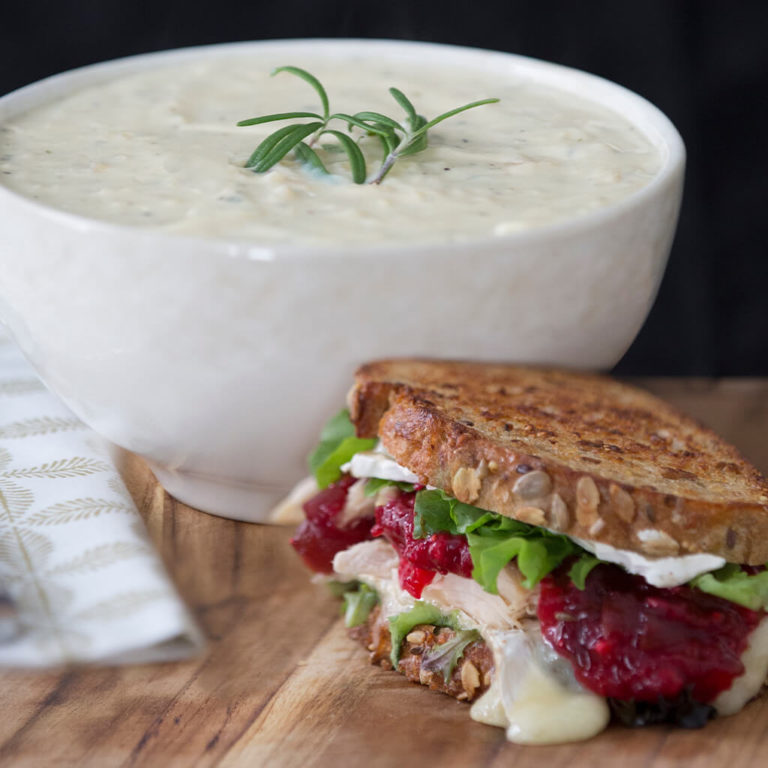 Delicious turkey cranberry sandwich with creamy soup and rosemary garnish, perfect for cozy meals.